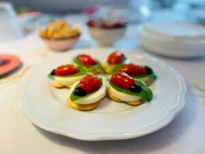 Creative ladybug-themed appetizers with tomatoes and olives on a white plate, perfect for parties.